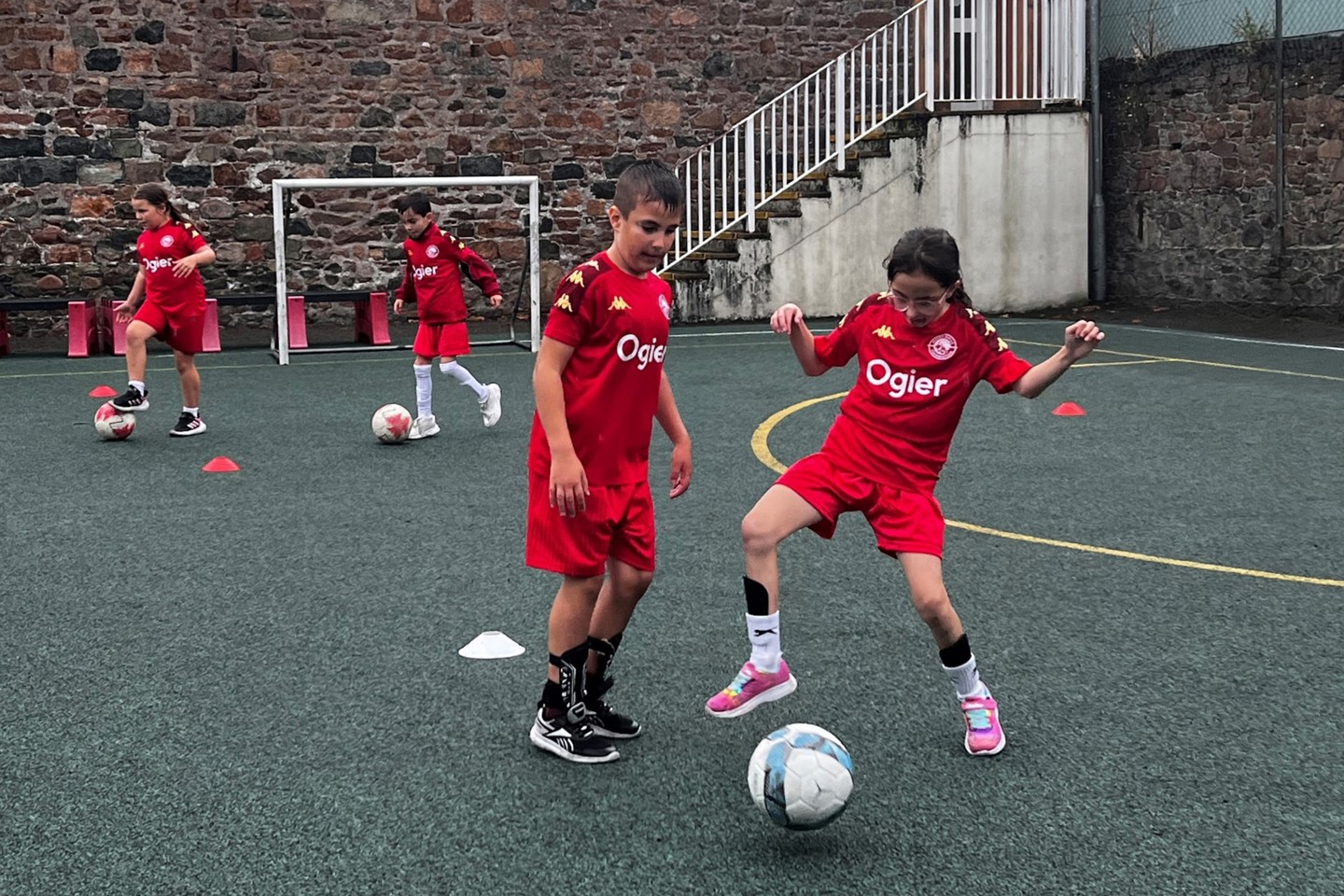 children in Ogier-branded football kits practise skills on an outdoor pitch as part of Jersey Bulls Community Foundation’s new after-school support programm