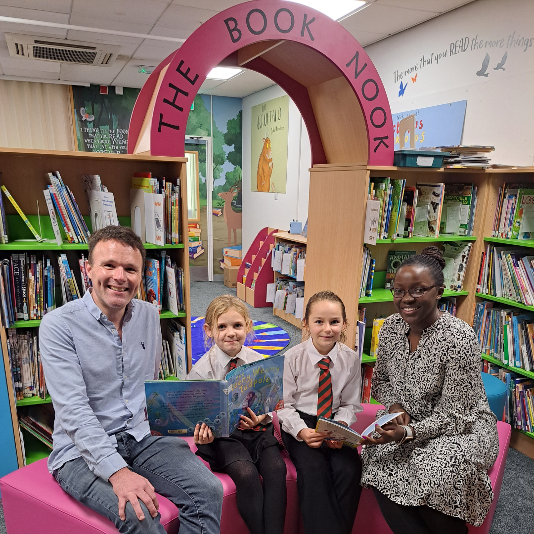 group of adults and school children in uniform enjoying storytelling together in a colourful library at Rouge Bouillon School in Jersey.