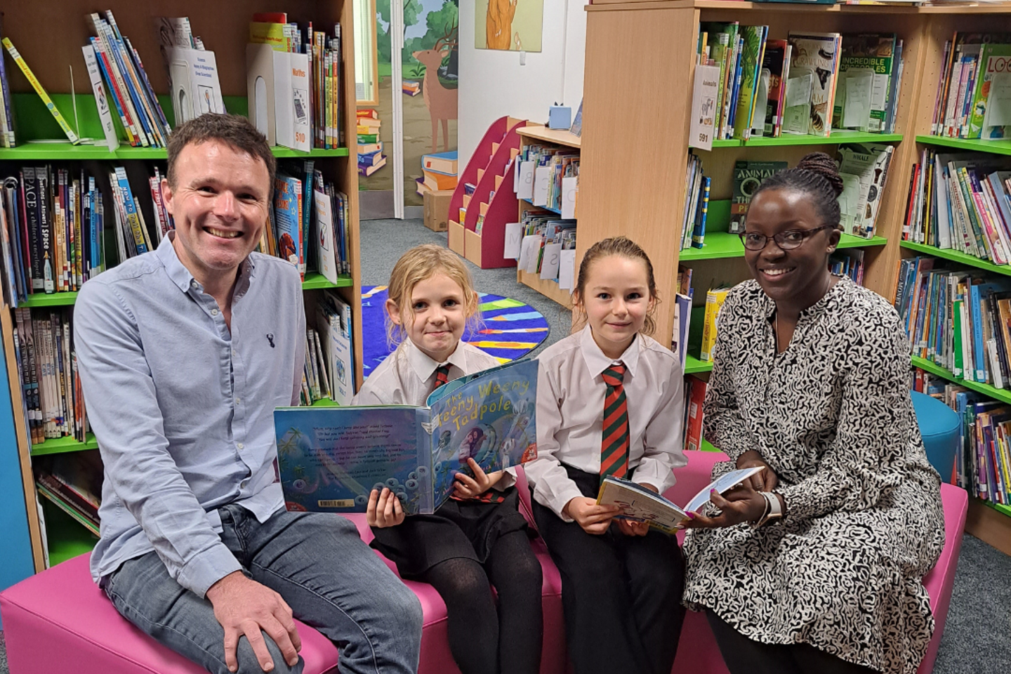 group of adults and school children in uniform enjoying storytelling together in a colourful library at Rouge Bouillon School in Jersey.